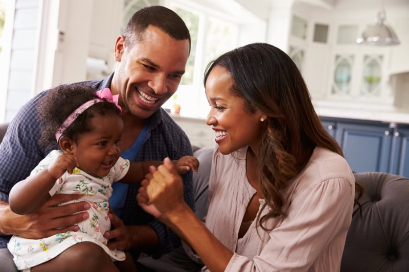 Happy parents playing with baby girl on dad's knee.